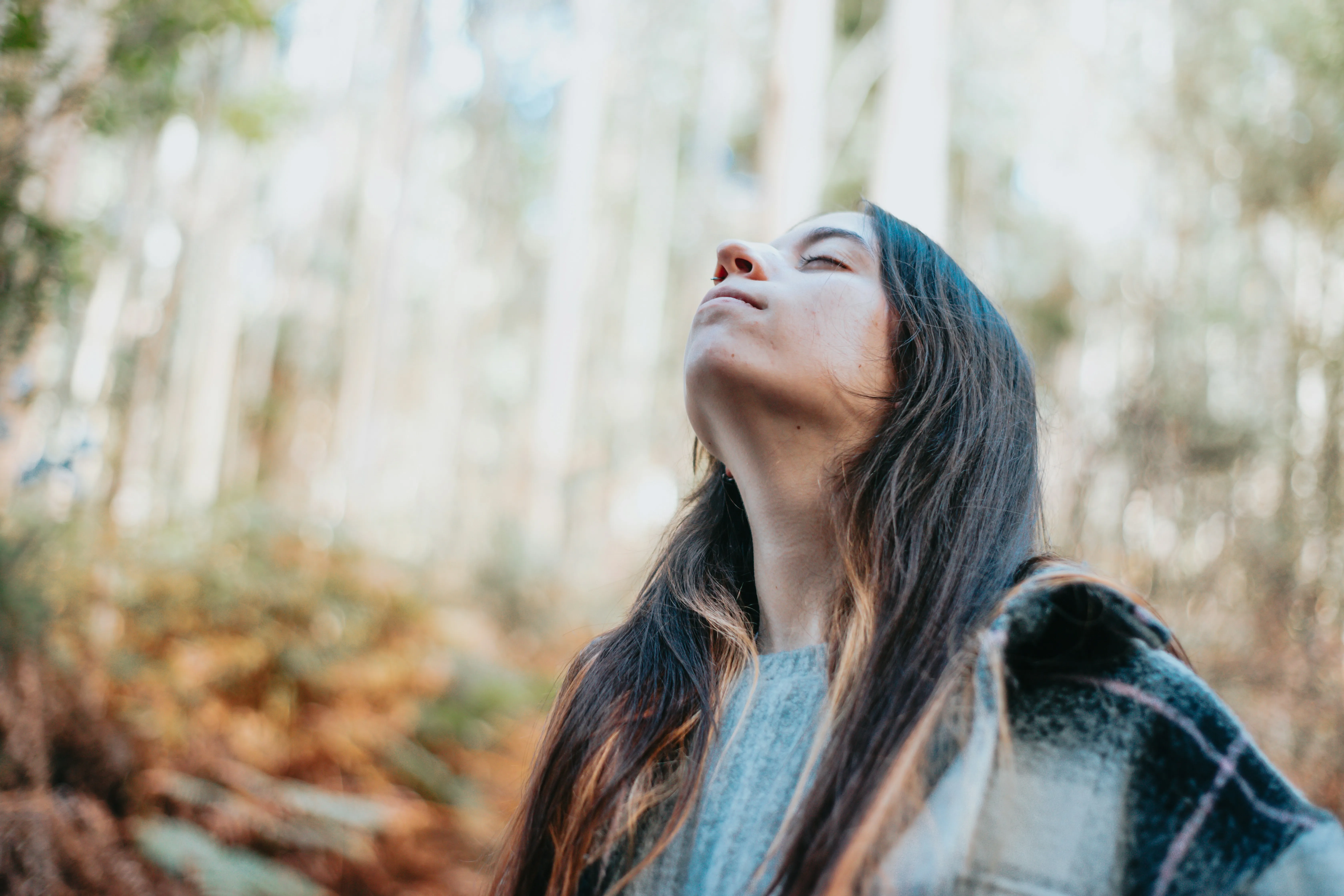 Woman breathing deeply in a sunlit forest, practicing the 4-7-8 breathing technique surrounded by trees