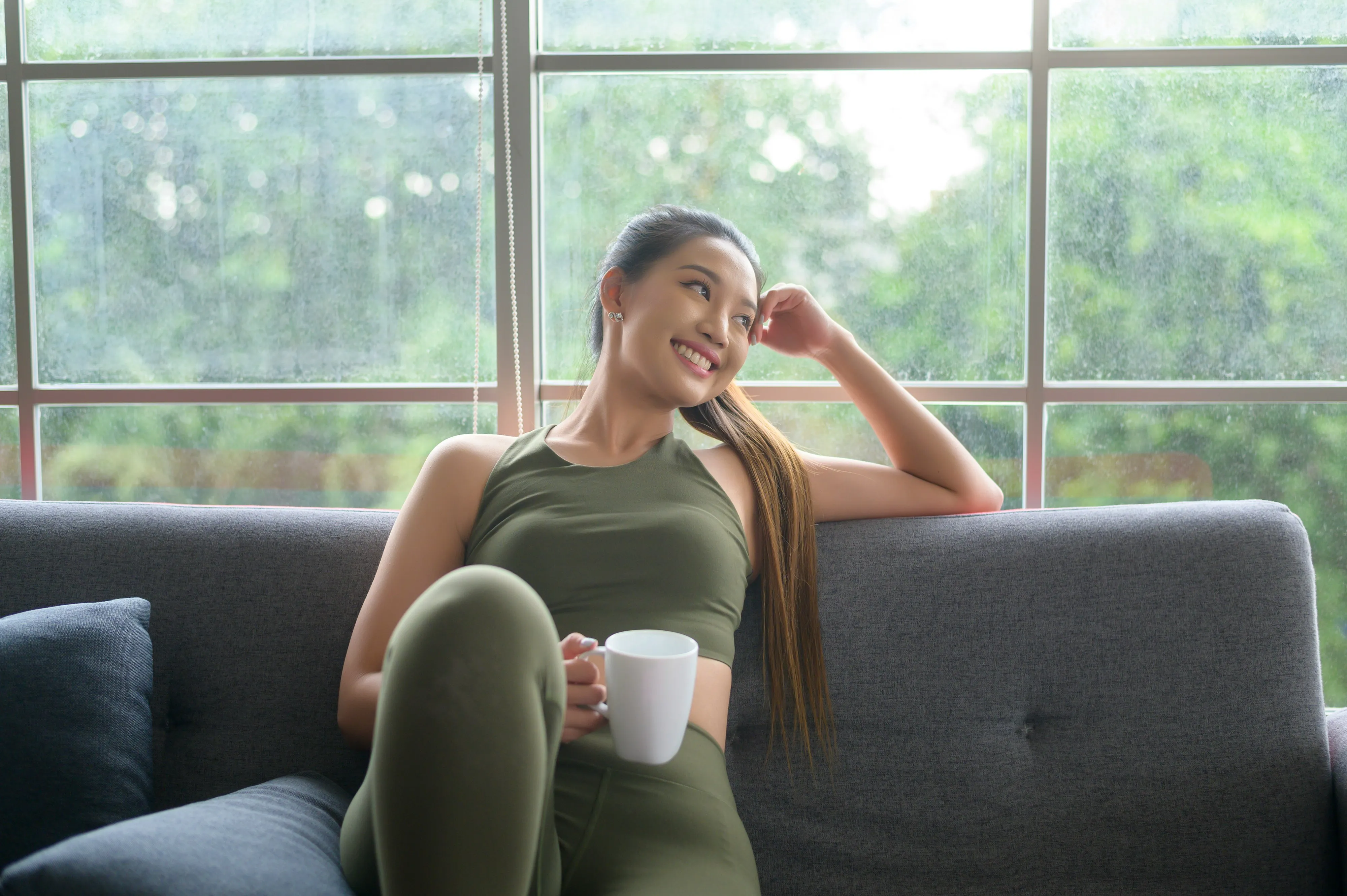 Woman in workout clothes relaxing on a couch with a cup of coffee, reflecting the connection between caffeine and exercise recovery