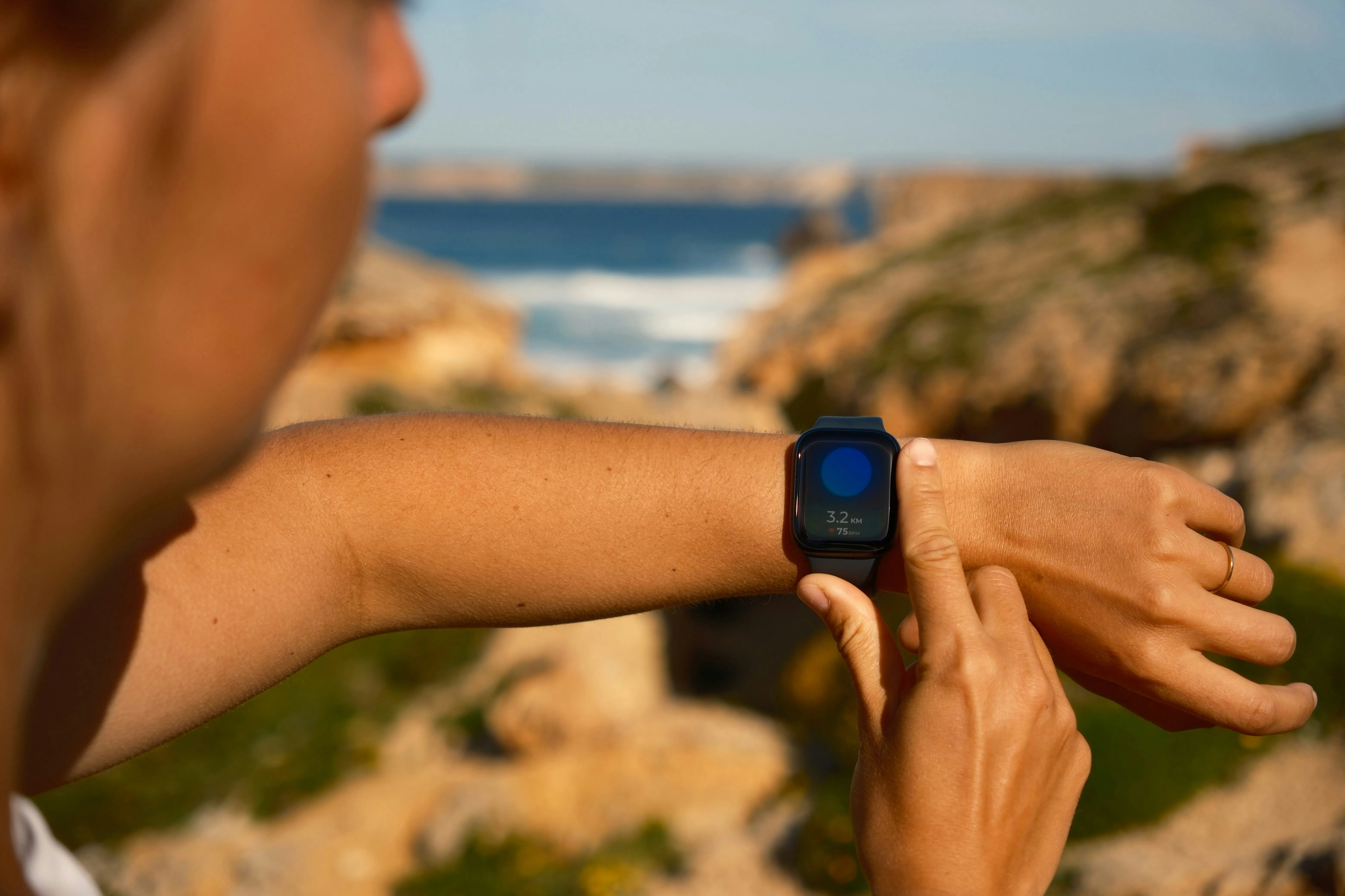 Person checking a smartwatch by the ocean, reviewing fitness tracking data outdoors