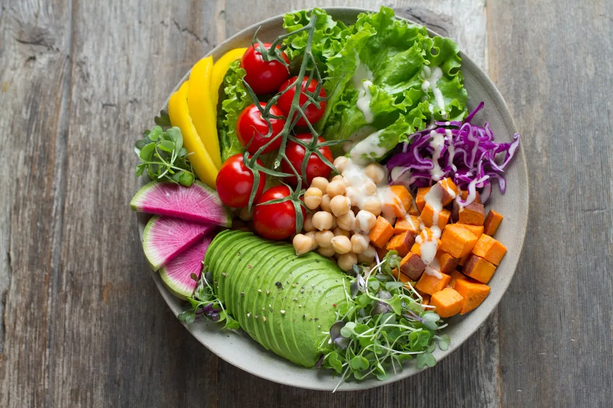 Colorful nutrition bowl with avocado, chickpeas, tomatoes, and leafy greens on a wooden surface