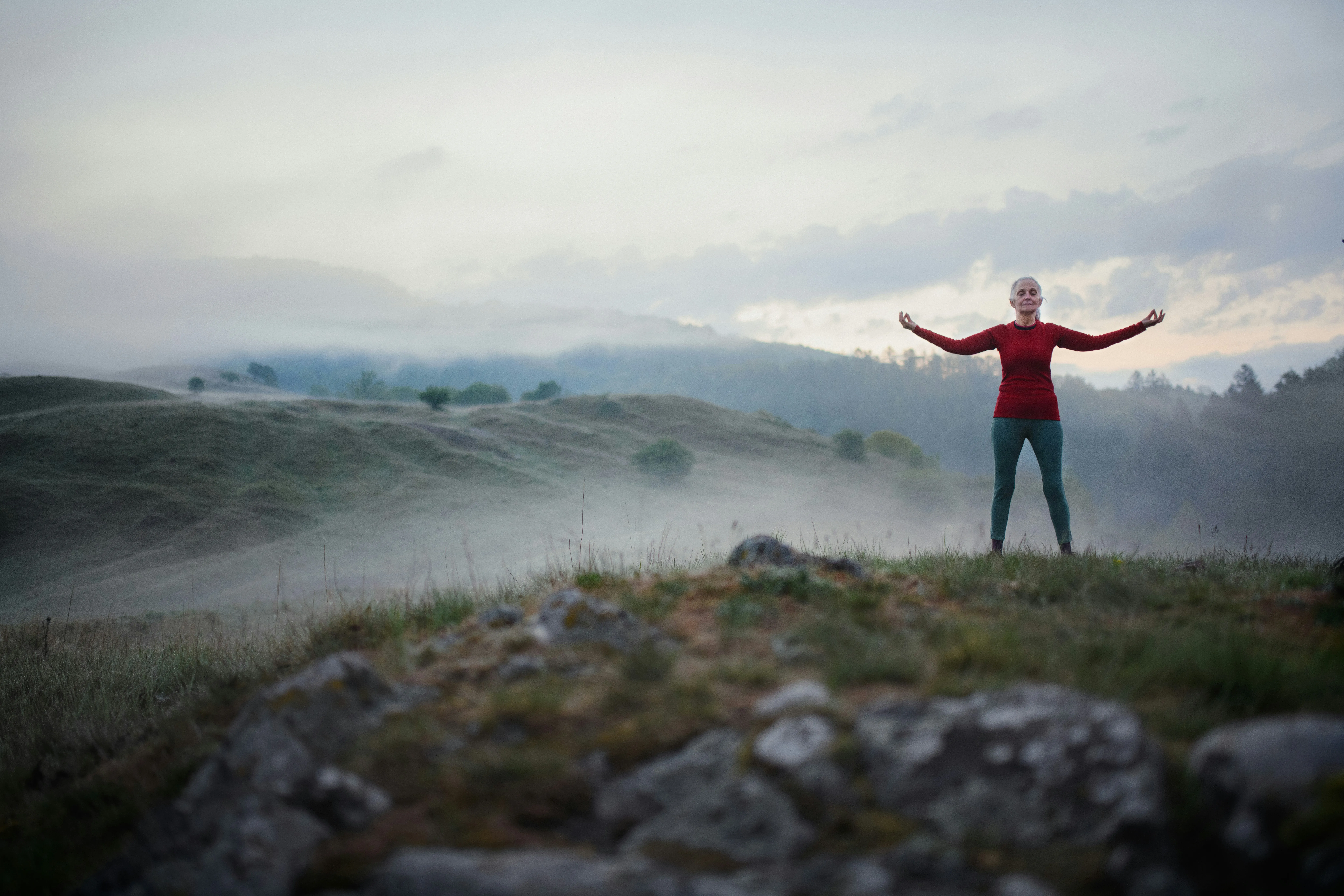 Woman standing with arms open on a misty hilltop, embracing the power of deep breathing