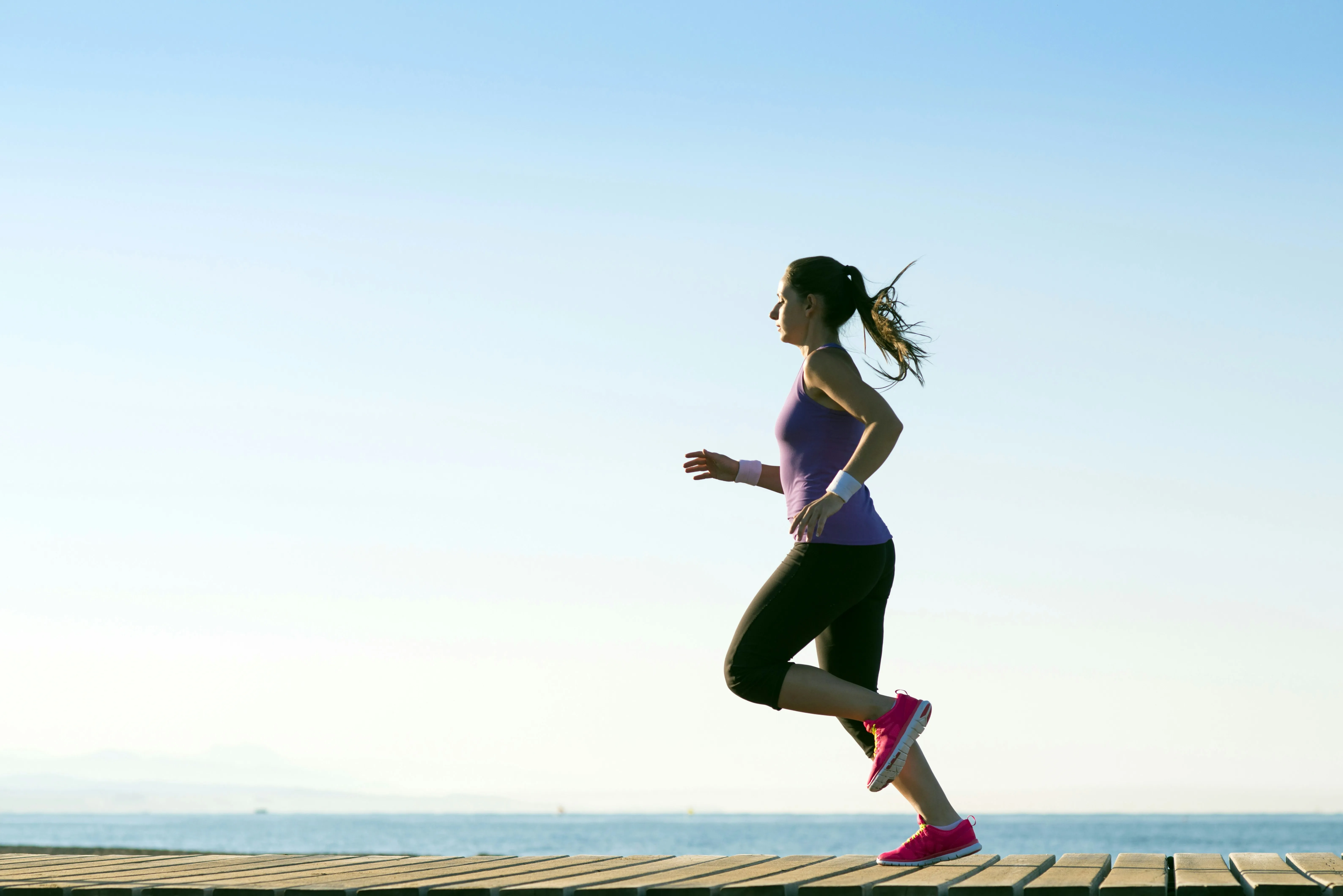 Woman jogging on a seaside boardwalk, building cardiovascular fitness to lower resting heart rate