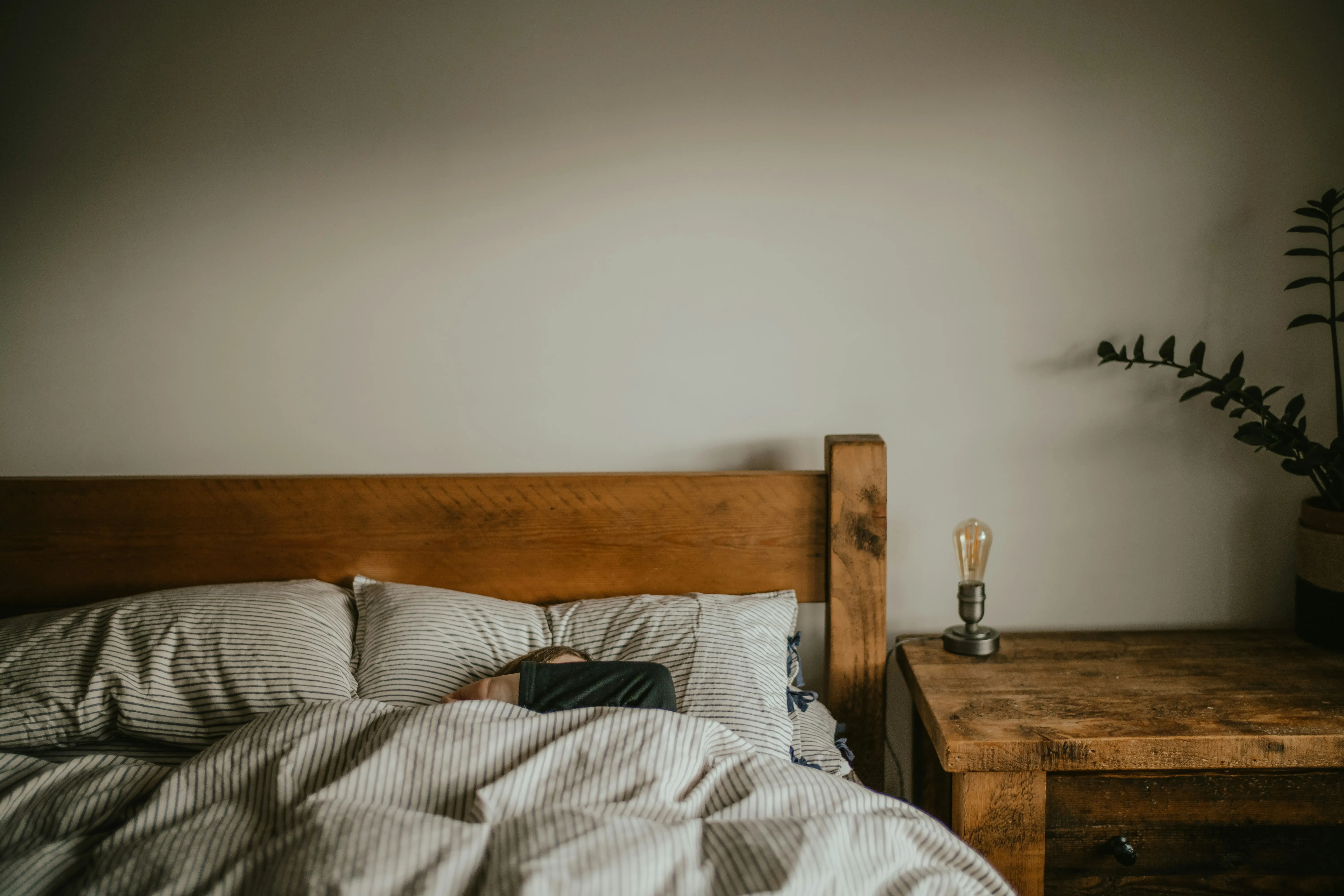 Cozy bed with striped linen sheets and a wooden headboard, emphasizing the importance of quality sleep for athletes