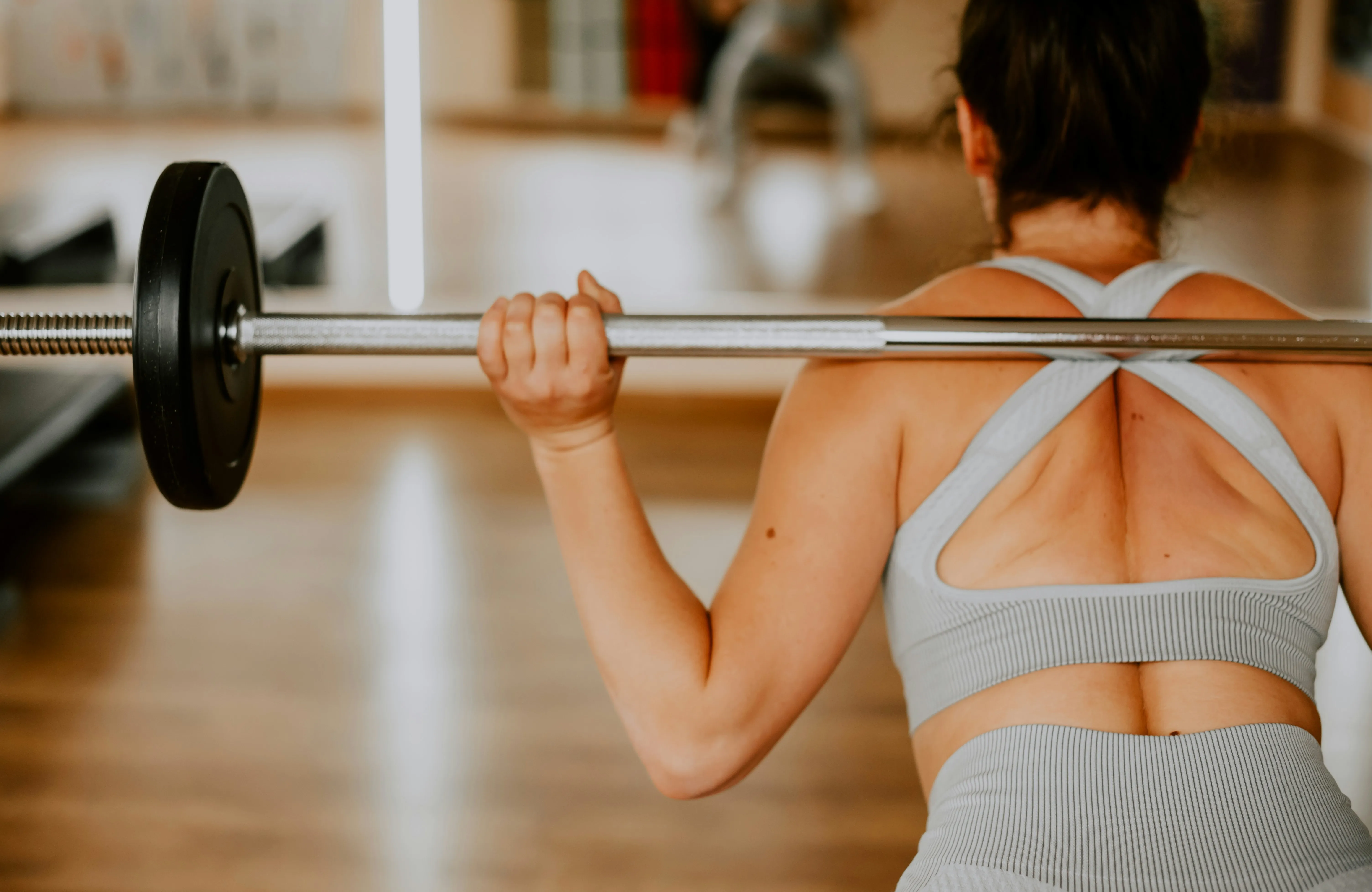 Woman holding a barbell on her shoulders in a gym, ready for a strength training session