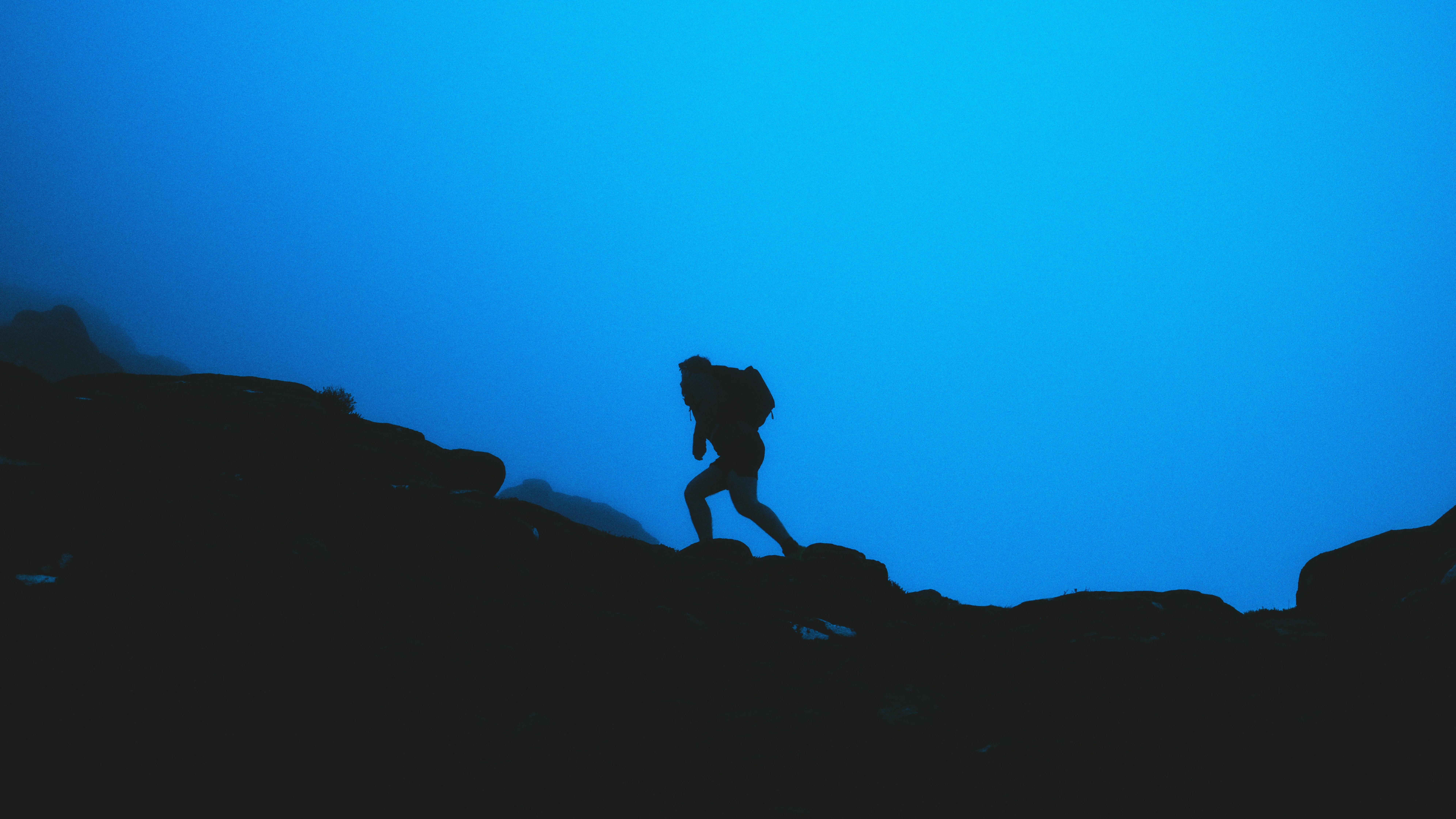 Silhouette of a hiker climbing rocky terrain against a blue dawn sky, symbolizing stress and performance